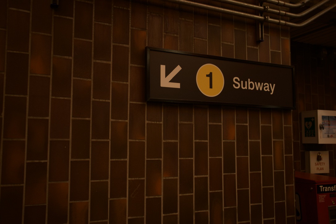 A warm-toned subway direction sign mounted on a tiled station wall.