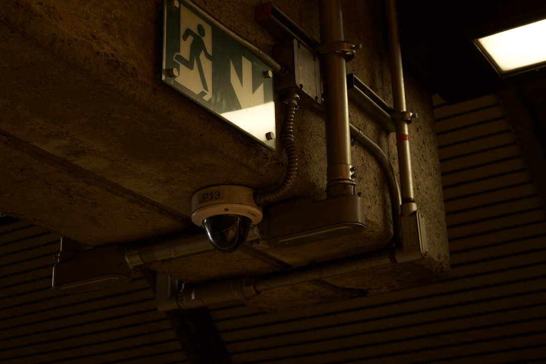 An illuminated exit sign, security camera and exposed station infrastructure.